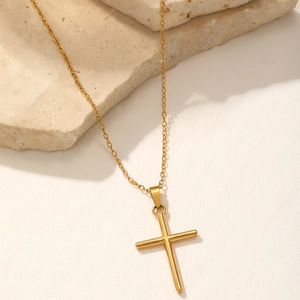 Close-up of a polished gold cross pendant on an elegant marble surface with warm lighting