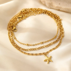 Close-up of three-layered gold ankle bracelets with starfish pendant on silk fabric