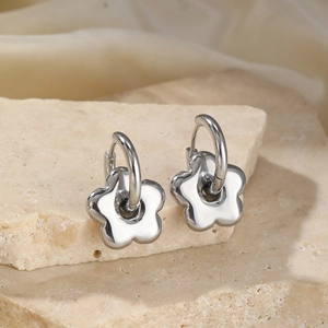 Boucles d'oreilles fleur en acier poli présentées sur pierre beige et tissu crème