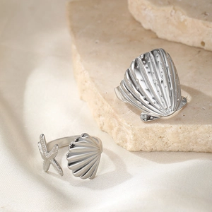 Detail of silver starfish and seashell rings on textured stone with silk background
