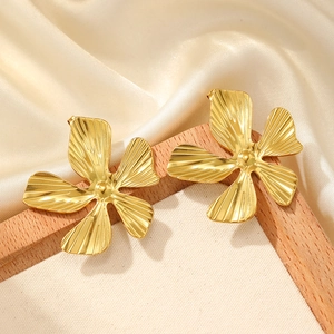 Detail of elegant gold flower earrings with radial textures on a silk background