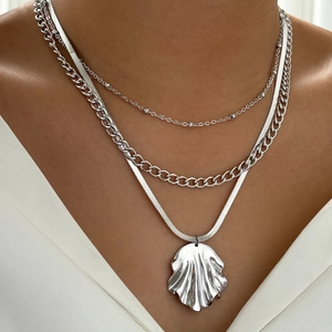 Detail of layered silver necklaces with beaded chains and a wavy geometric pendant