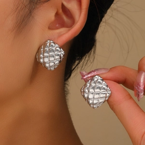 Detailed view of silver square quilted metal stud earrings worn by a model in soft light