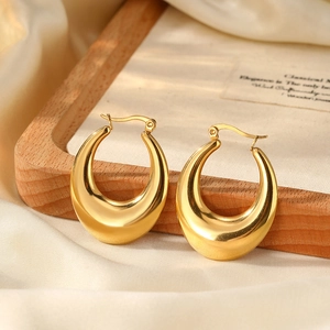 Macro detail of high-polish gold teardrop hoop earrings on elegant silk fabric