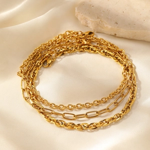 Detailed view of layered gold anklet set featuring Figaro chains on premium silk fabric