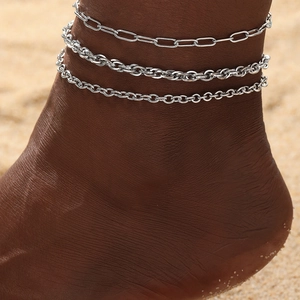 Three-piece silver anklet set featuring layered paperclip and link chains on model's ankle