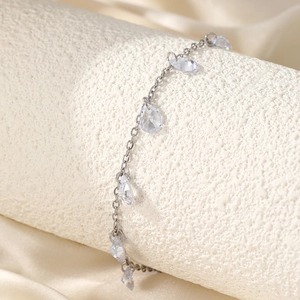 Detailed shot of silver anklet featuring teardrop zircons on champagne silk background