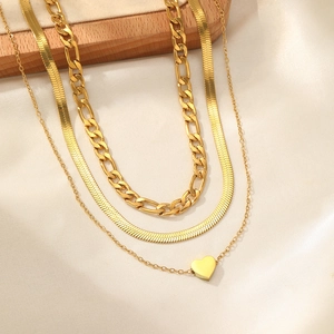 Close-up of layered gold necklace set with Figaro chain, snake chain and heart pendant
