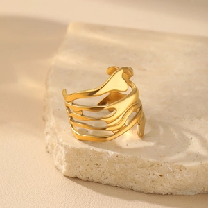 Detail of gold-plated irregular wavy ring placed on a textured stone with shadows