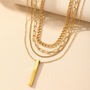 Détail de colliers dorés superposés avec divers styles de chaînes et un pendentif barre lisse