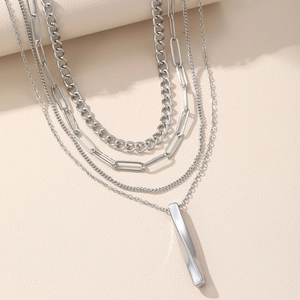 Collier à maillons multicouches avec pendentif barre en métal torsadé sur fond beige