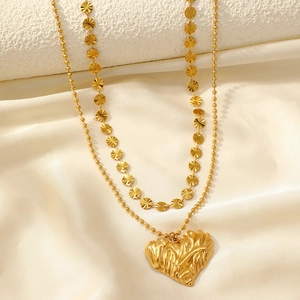 Dettaglio di una collana doppia dorata con ciondolo a cuore ondulato su sfondo di seta