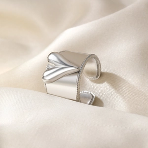 Détail de la bague coeur argentée aux bords tressés sur fond de soie blanche