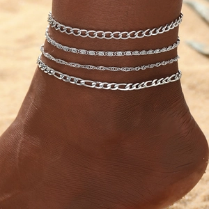 Detail of a four-piece layered silver anklet set with cuban and rope chains on beach ankle
