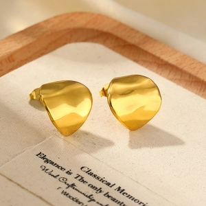Detail of golden irregular geometric stud earrings with hammered metal texture on linen