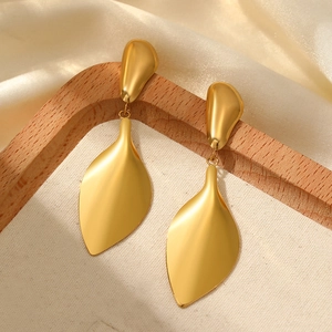 Detail of golden matte leaf drop earrings on a textured cream display stand