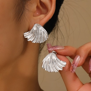 Détail des boucles d'oreilles argentées en forme de coquillage à texture plissée