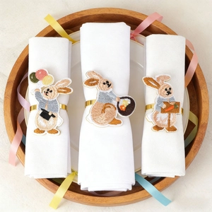 Detailed close-up of embroidered rabbit napkin rings on white linens for table setting