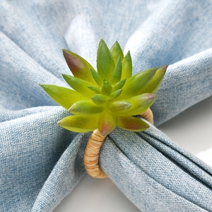 Faux succulent plant napkin ring with woven natural ring on a light blue table napkin