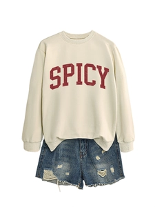 Close-up of cream crewneck sweatshirt featuring red Spicy print and distressed denim shorts