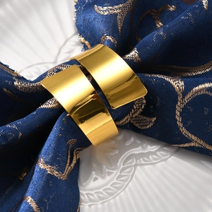 Macro detail of polished gold napkin rings on blue embroidered fabric and white plate