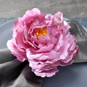 Close-up of pink peony floral napkin ring with yellow stamens on dark grey silk fabric
