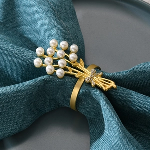 Nahaufnahme vom goldenen Rosen-Serviettenring mit weißen Perlen und Strassschleife