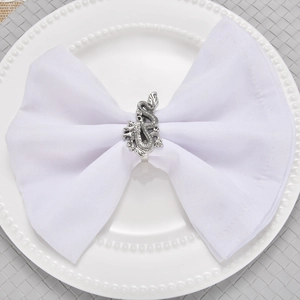 Detailed close-up of a silver dragon napkin ring on a white napkin and ceramic plate
