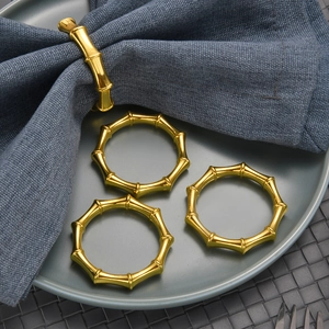 Set of 4 gold bamboo-style napkin rings displayed on a blue linen napkin and green plate