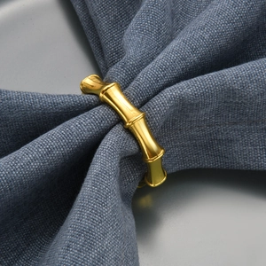 Polished gold bamboo-style metal napkin ring on textured blue fabric background