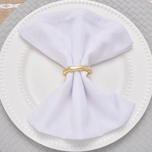 Close-up of golden bamboo design napkin ring on white fabric napkin and beaded ceramic plate