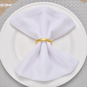 Close-up of a gold bamboo-shaped metal napkin ring on a white napkin and decorative plate