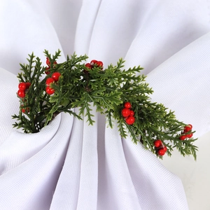 Detail of Christmas napkin ring featuring artificial pine needles and red berries on a napkin