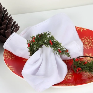 Christmas napkin ring with pine needles and red berries on a festive white table setting