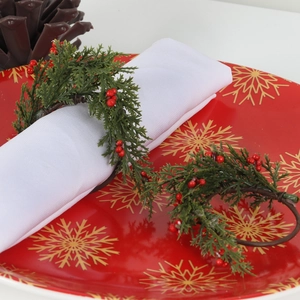 Handmade Christmas napkin rings with green pine needles and red berries on a festive red plate