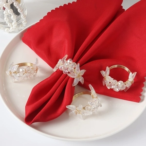 Set of four gold wire napkin rings with crystal leaf charms on a red napkin and plate