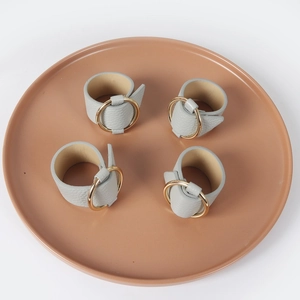 Set of four grey PU leather napkin rings with polished gold buckles on a ceramic plate