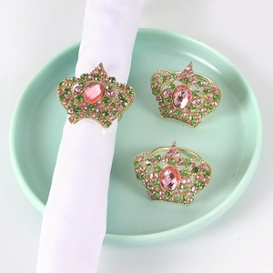 Detail of golden crown napkin ring with pink and green crystals on white fabric