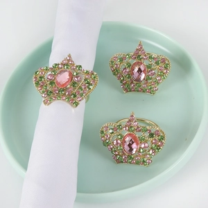 Macro shot of crown napkin rings with pink and green crystals on mint green plate