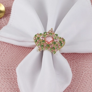Elegant gold crown napkin ring with pink and green crystals on white satin fabric