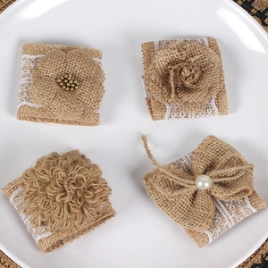 Detail of four handmade burlap napkin rings with white lace and pearls on a white plate