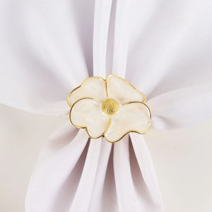 Close-up of white enamel flower napkin ring with gold trim on white fabric