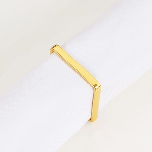 Detalle de un servilletero rectangular dorado pulido espejo sobre una servilleta blanca