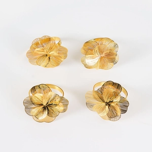 Dettaglio di quattro portatovaglioli dorati con fiori multistrato e petali in metallo traforato