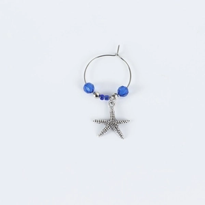 Close-up of a silver starfish wine glass charm with blue beads on a metal ring