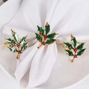 Detailed view of green enamel holly leaf napkin ring with red rhinestones on a white napkin