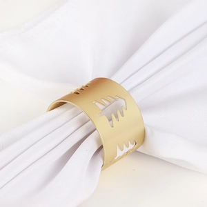 Detail of matte gold napkin ring featuring hollow Christmas tree patterns on white napkin
