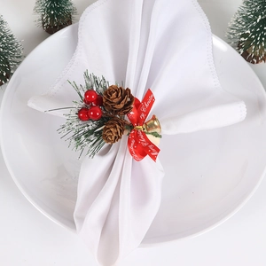 Detail of Christmas napkin ring with pine cones, red berries and gold bell on a plate