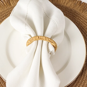 Servilletero de mimbre tejido a mano sobre servilleta blanca con textura de madera natural