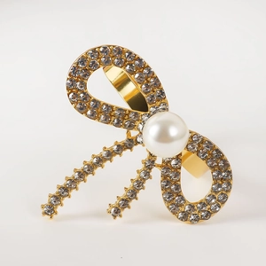 Close-up of golden bow-shaped napkin ring with sparkling rhinestones and a white pearl